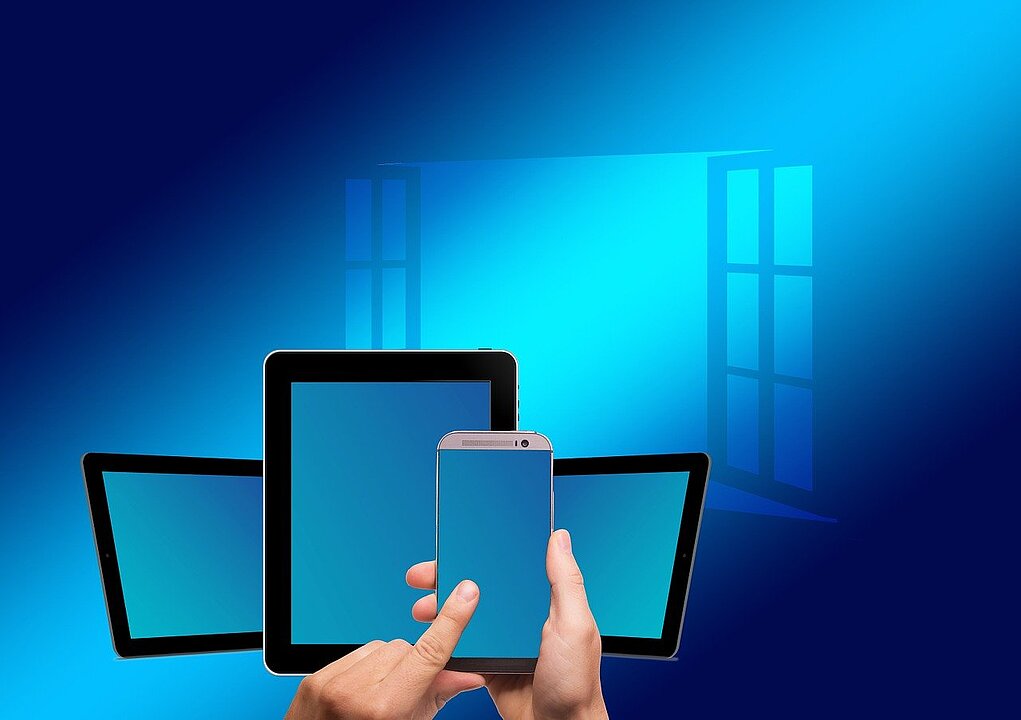 Im Vordergrund Hand, die ein Smartphone hält und darauf tippender Finger. Im Hintergrund offenes Fenster.